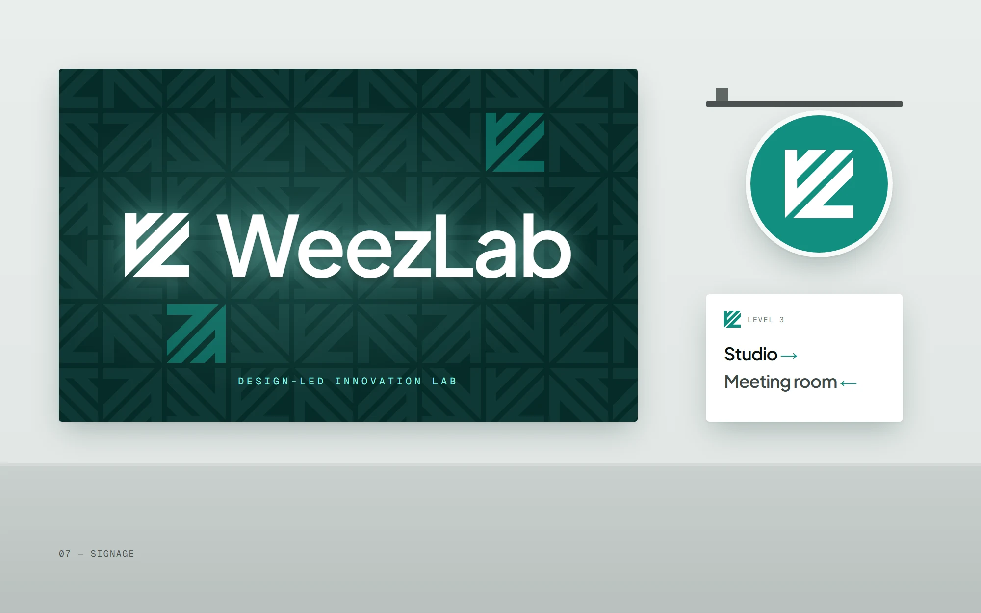Studio signage: a backlit WeezLab logo on a deep teal patterned wall, a round teal blade sign with the logomark, and a white wayfinding plaque.